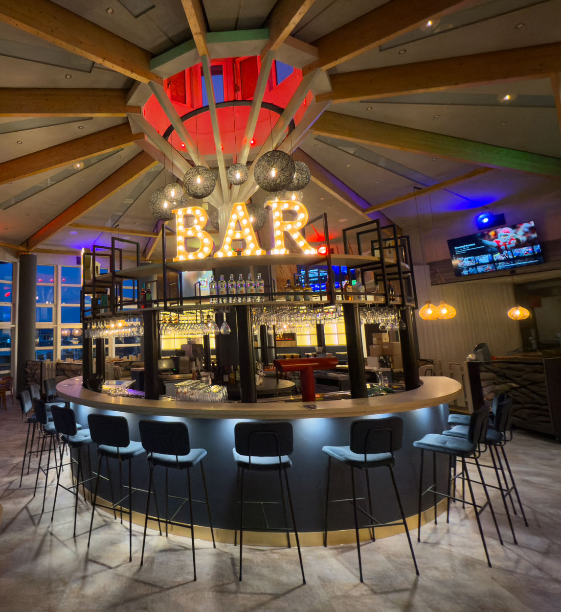 StormyBar mit rundem Tresen, hohen Barhockern und beleuchtetem „BAR“-Schild.