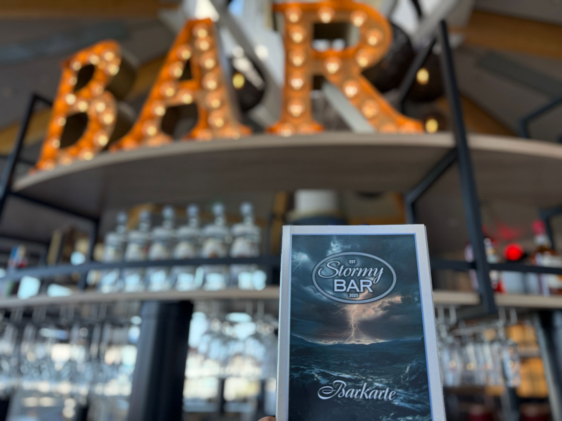Beleuchtetes "BAR"-Schild und einer Speisekarte der StormyBAR im Vordergrund.