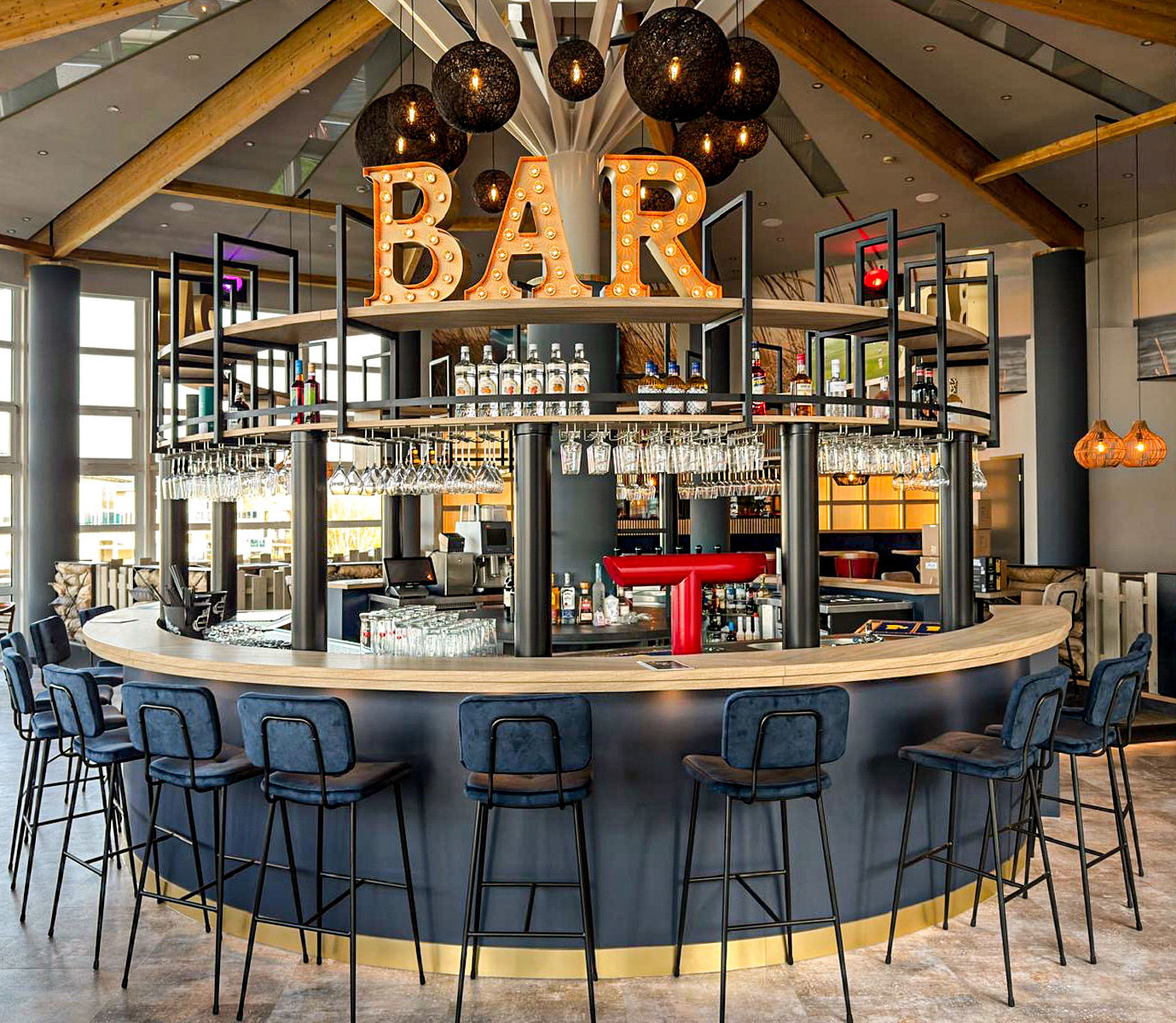 Runde StormyBAR in modernem Raum mit Leuchtschrift "BAR" und schwarzen Stühlen.