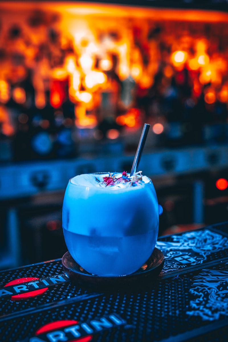 Weiße Cocktailkugel mit Strohhalm auf einer Bar, leuchtender Hintergrund.